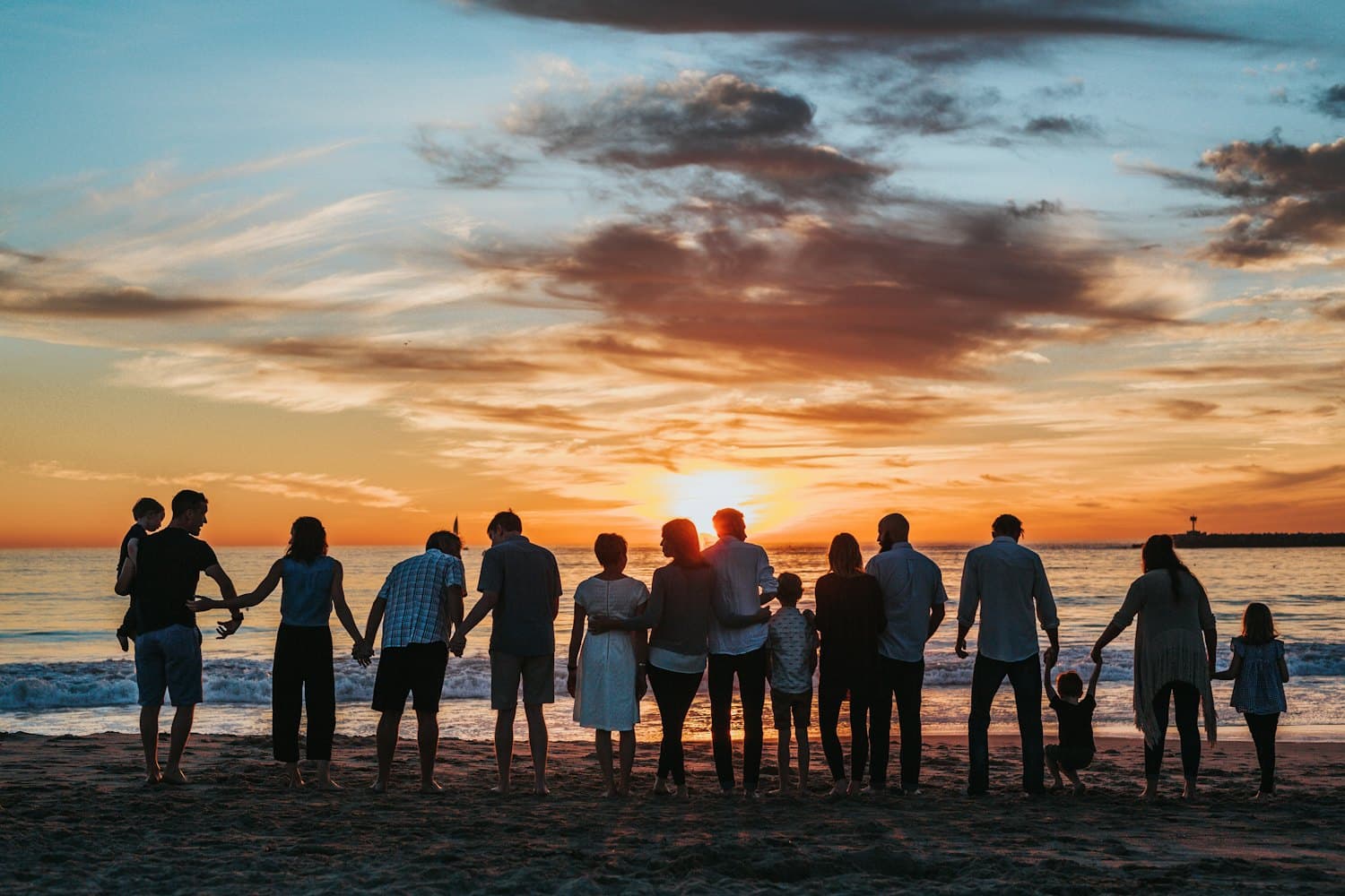 Wielopokoleniowa rodzina trzyma się za ręce na plaży o zachodzie słońca